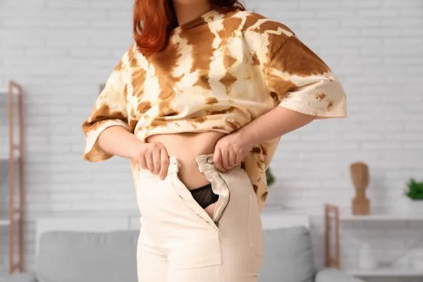 Image of woman trying to do her trousers up after pregnancy weight gain Cheadle